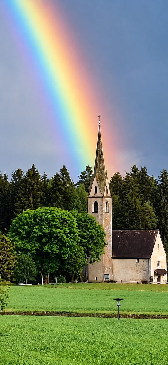 Regenbogen über einer Kirche am Weg als Sinnbild für Hoffnung